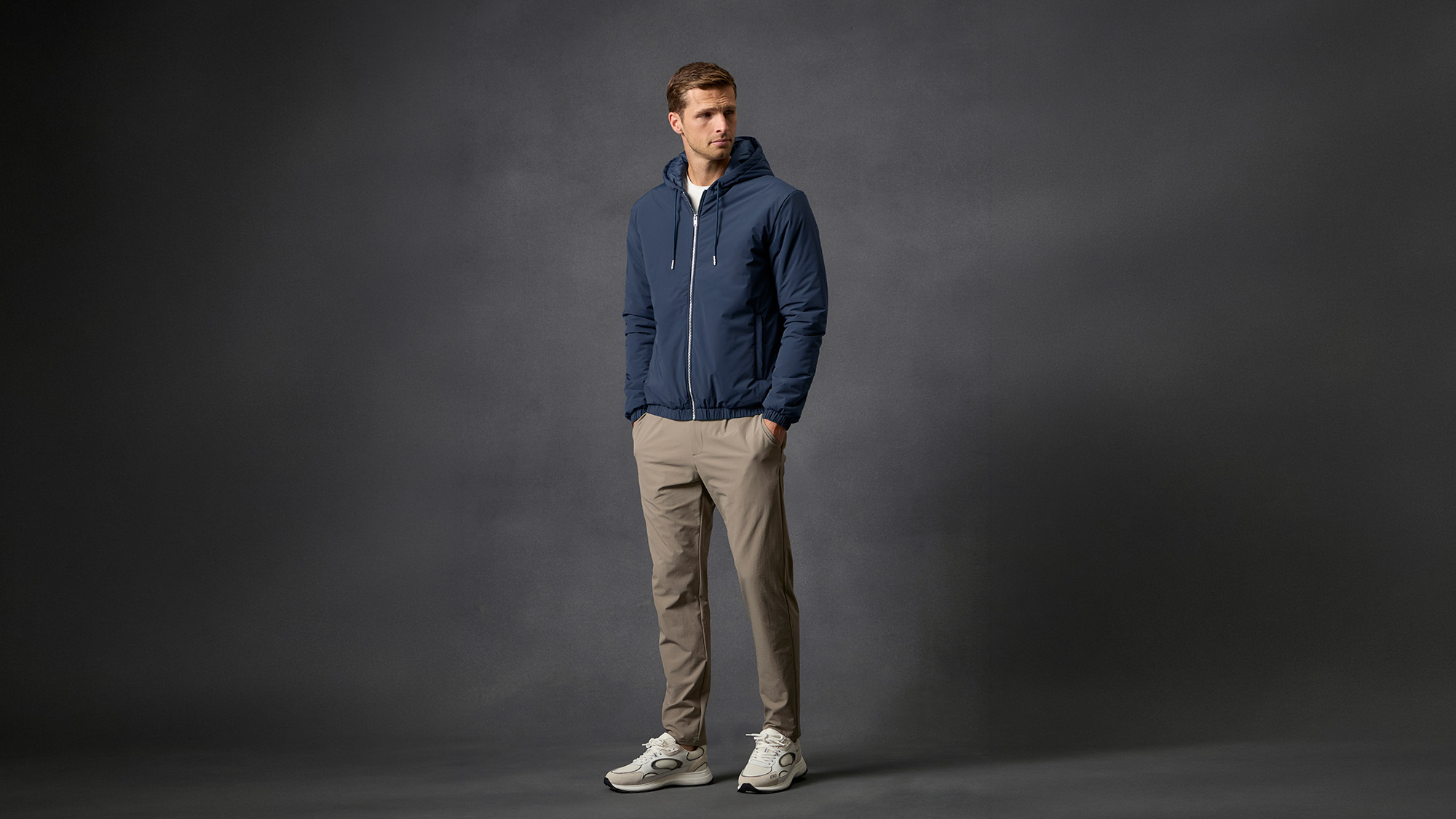 Man wearing navy hooded jacket and beige trousers with white trainers, Arne everyday essentials collection