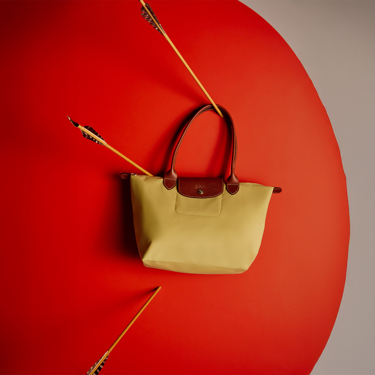 A beige handbag with brown handles is mounted on a red background, pierced by three arrows.
