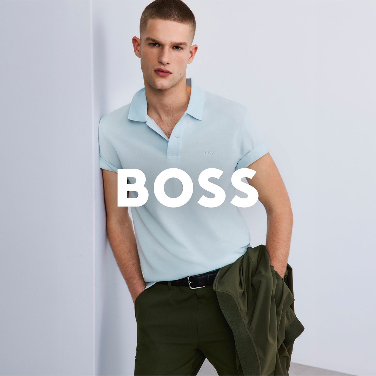 Man wearing light blue polo shirt and olive trousers against neutral background with BOSS text overlay