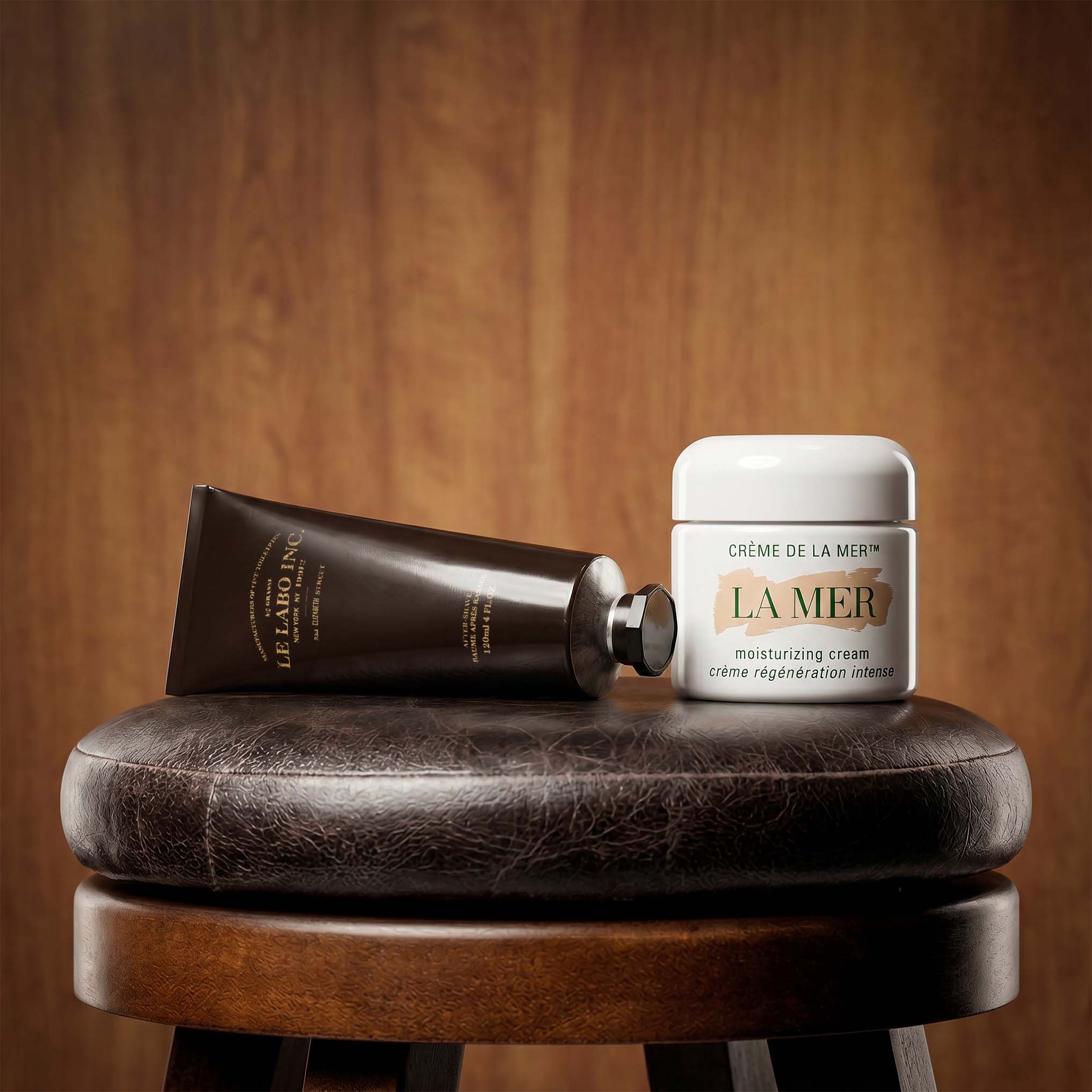 La Mer moisturising cream and dark grooming product displayed on textured leather surface against warm wood backdrop
