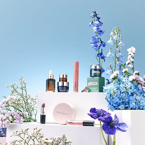 Cosmetics and skincare products arranged among vibrant flowers against a blue background.