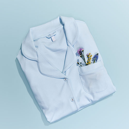 Folded light blue pajama top with wildflowers in the pocket, on a light blue background.