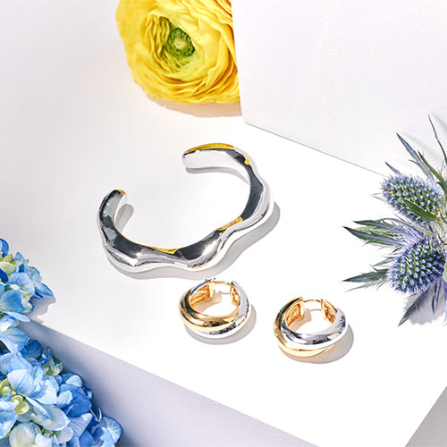 Silver jewelry set with a bracelet and rings placed amidst yellow, blue, and purple flowers on a white background.
