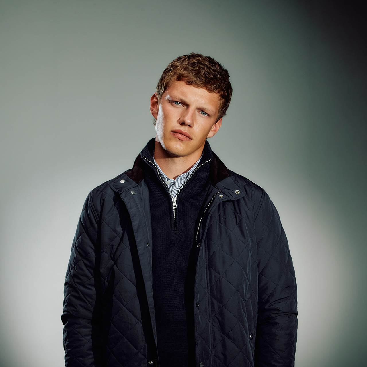 Man wearing navy quilted jacket over navy knit with striped shirt collar visible