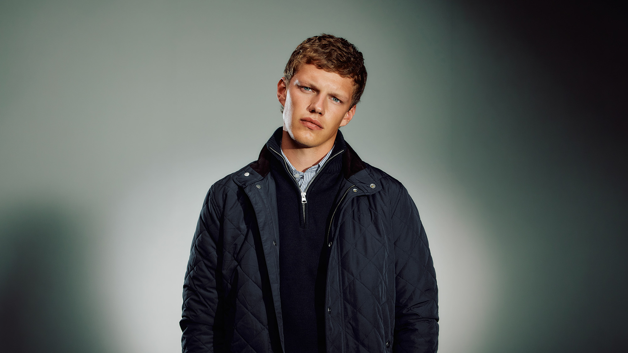 Man wearing navy quilted jacket over navy knit with striped shirt collar visible