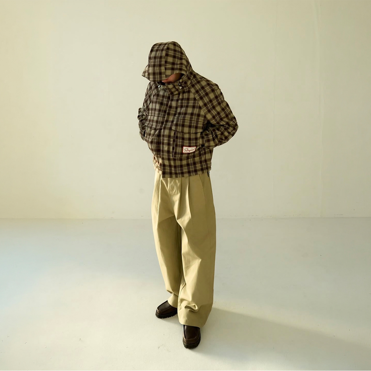 Man wearing brown and cream checked hooded jacket with cream wide-leg trousers and dark shoes