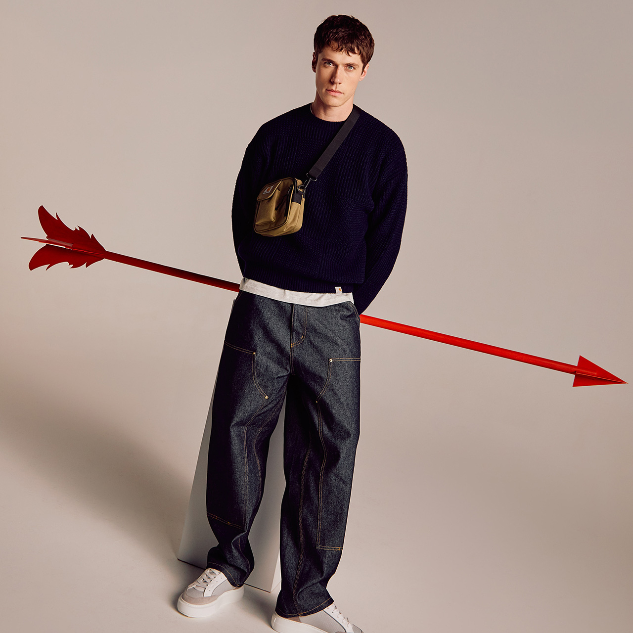 A man stands in casual attire with a large red arrow appearing to pass through him, set against a plain background.