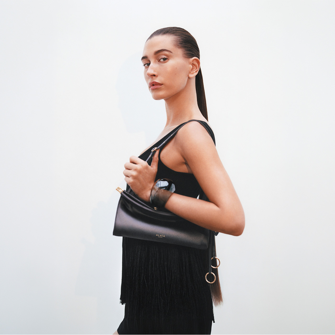 Woman wearing black sleeveless top and fringed skirt, carrying black leather shoulder bag
