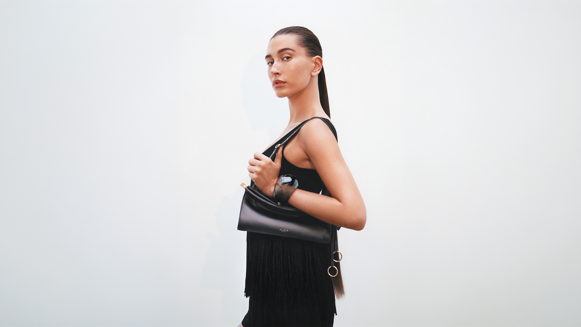 Woman wearing black sleeveless top and fringed skirt, carrying black leather shoulder bag