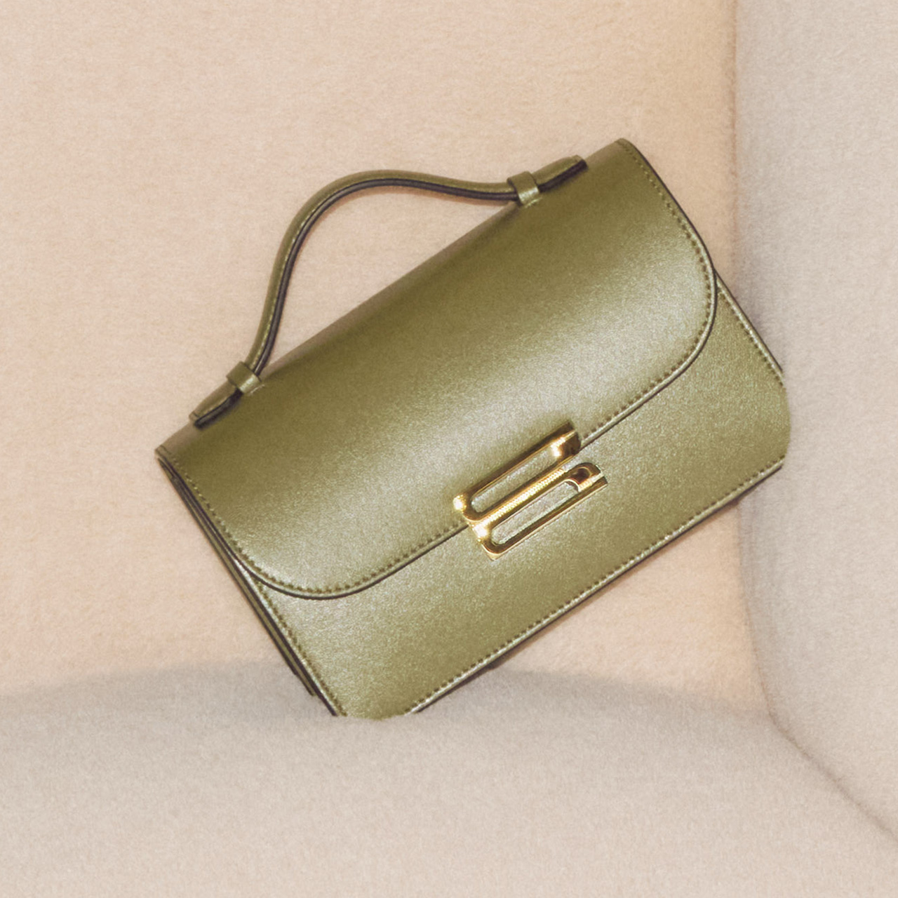 Olive green leather shoulder bag with gold hardware on neutral fabric background