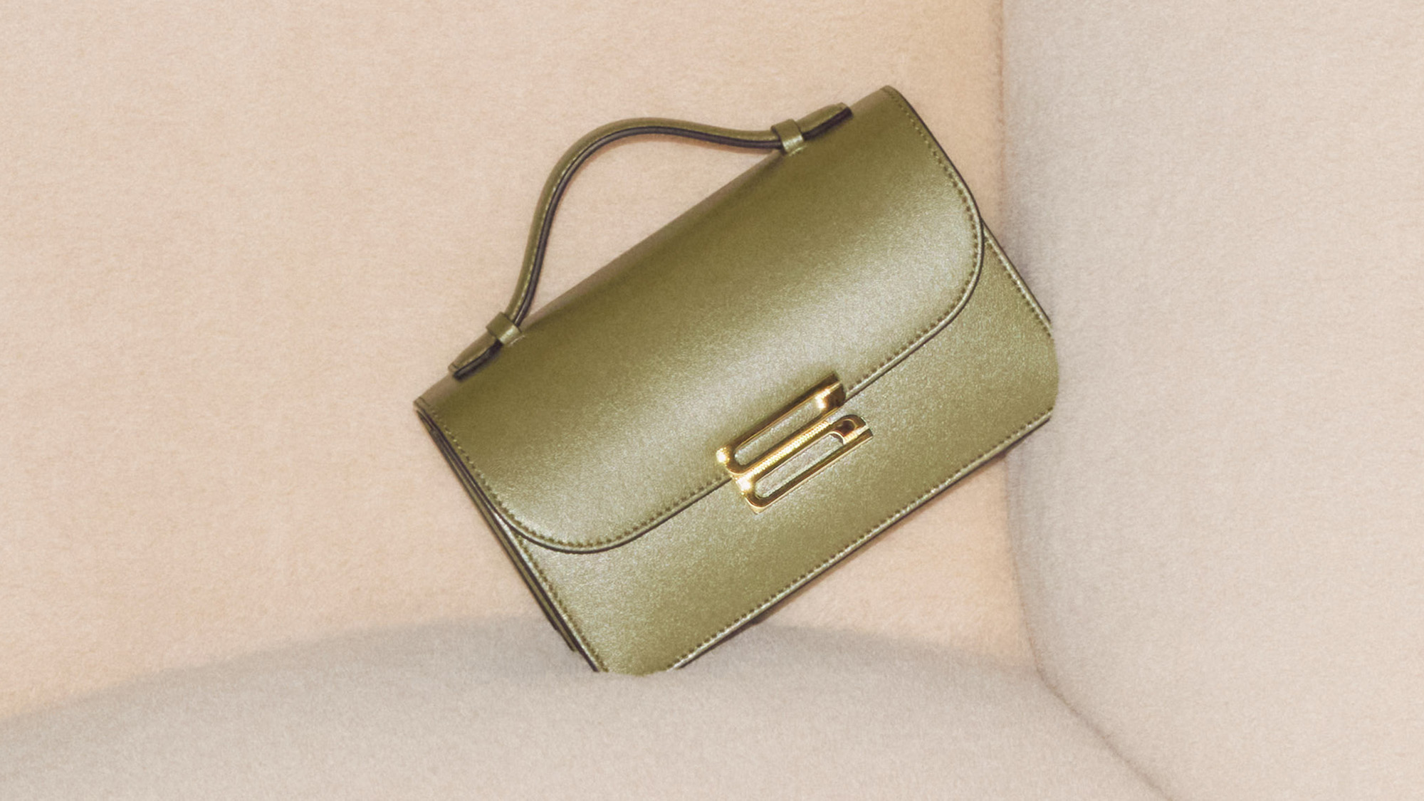 Olive green leather shoulder bag with gold hardware on neutral fabric background