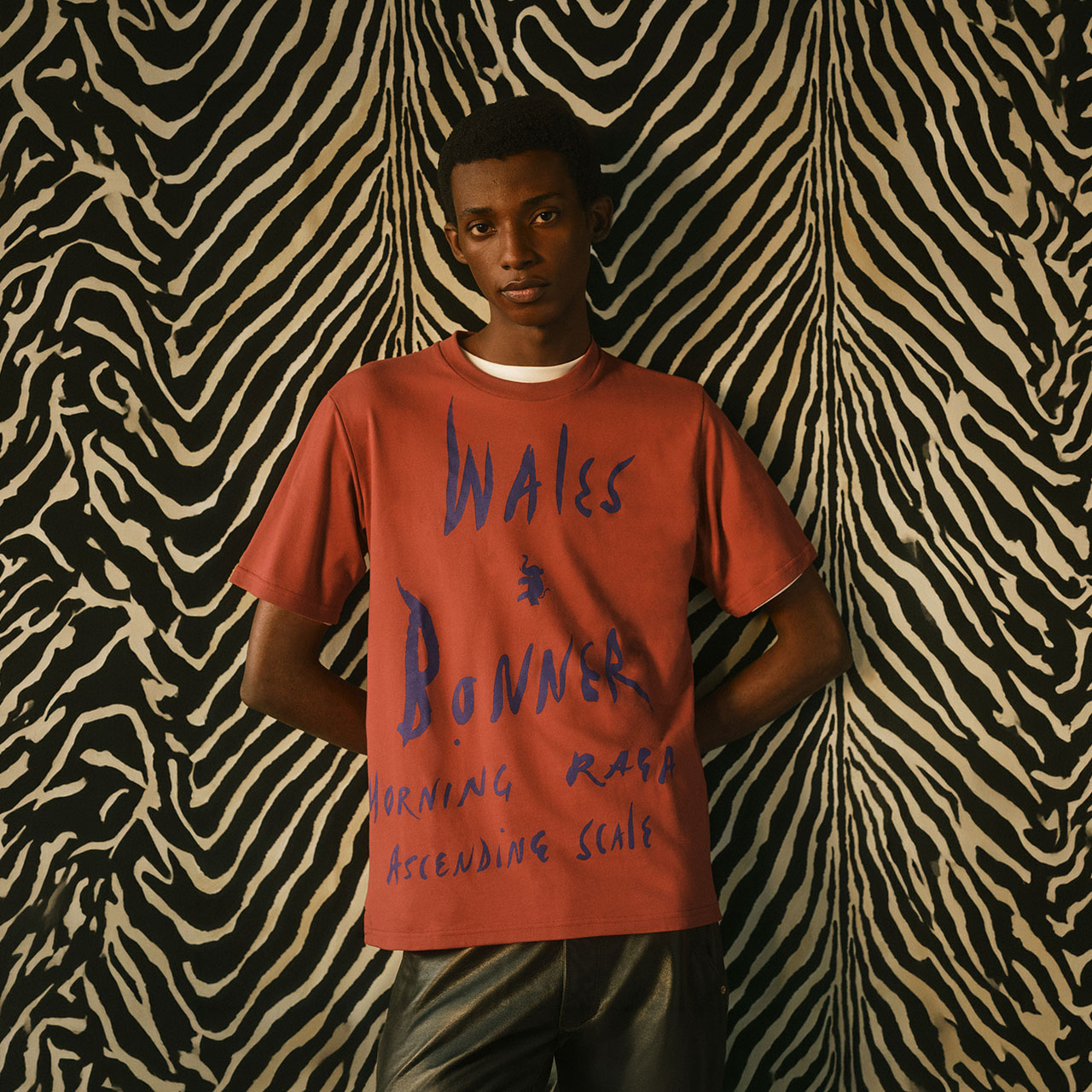 Man wearing rust-coloured t-shirt with blue text against zebra-striped background
