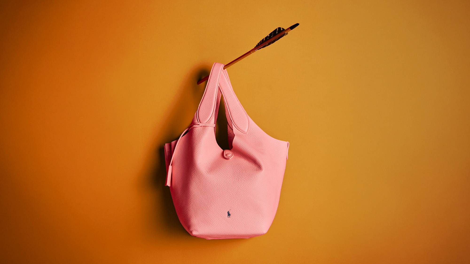 A pink tote bag pierced by an arrow against an orange background.