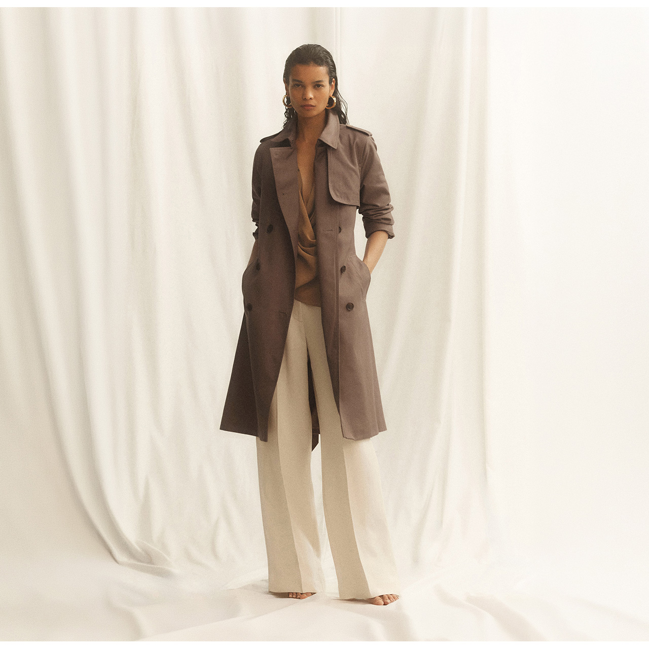 Woman wearing brown trench coat over brown top and cream wide-leg trousers