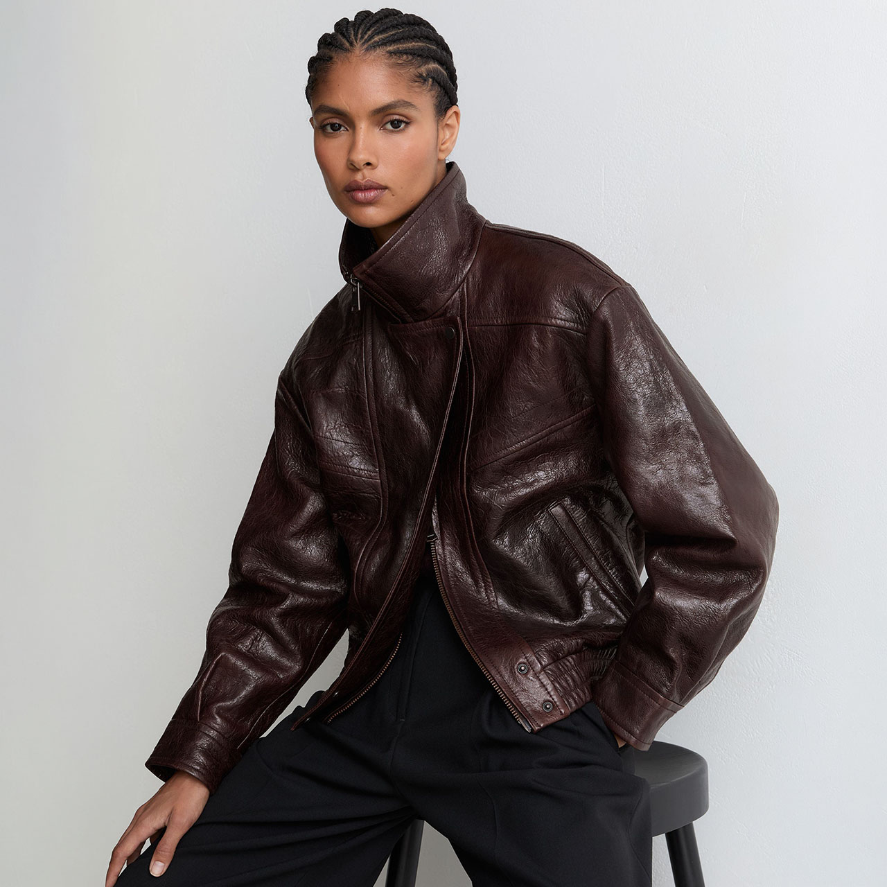 Woman wearing burgundy leather jacket with high collar and zip fastening against neutral background