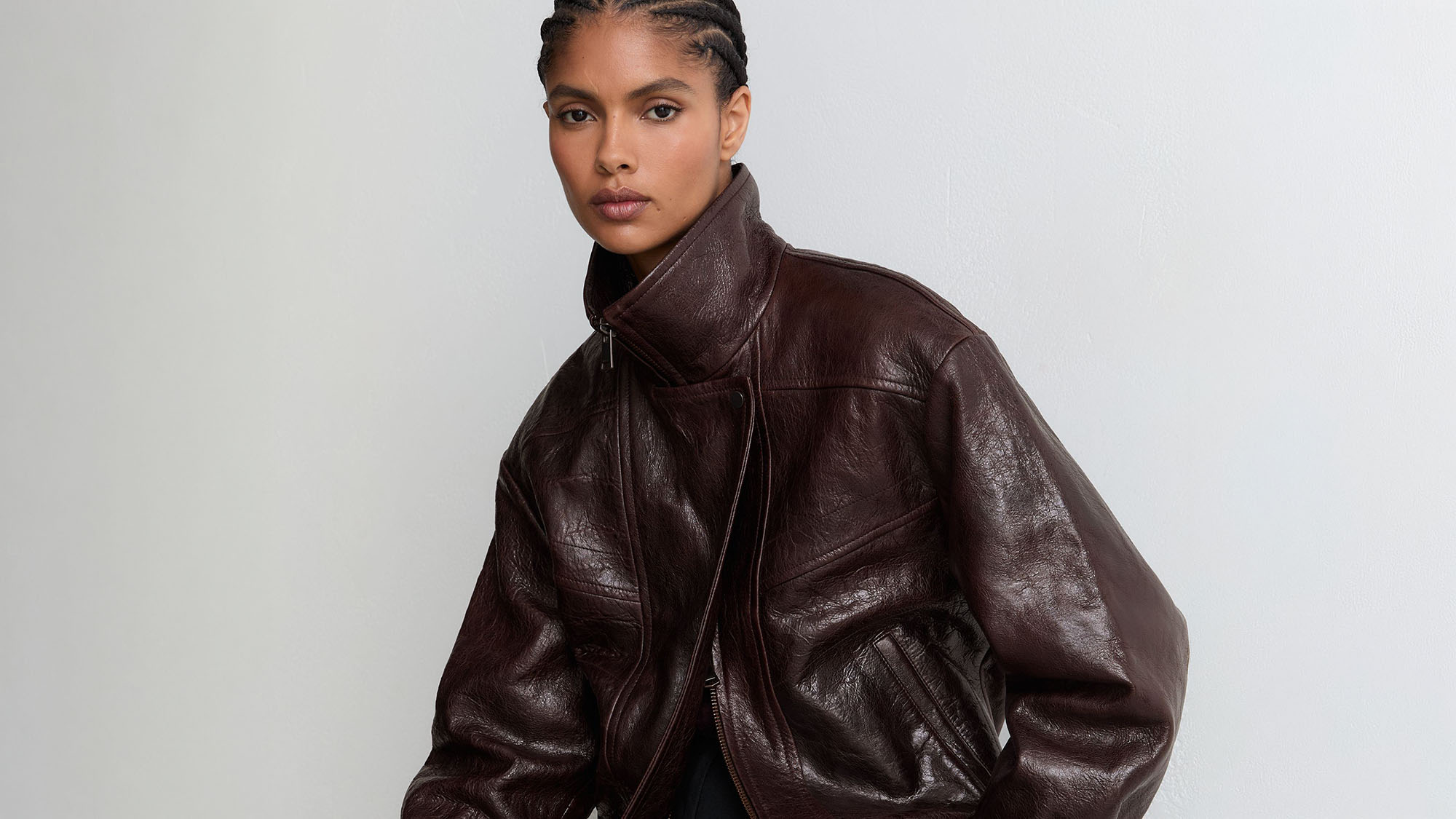 Woman wearing burgundy leather jacket with high collar and zip fastening against neutral background