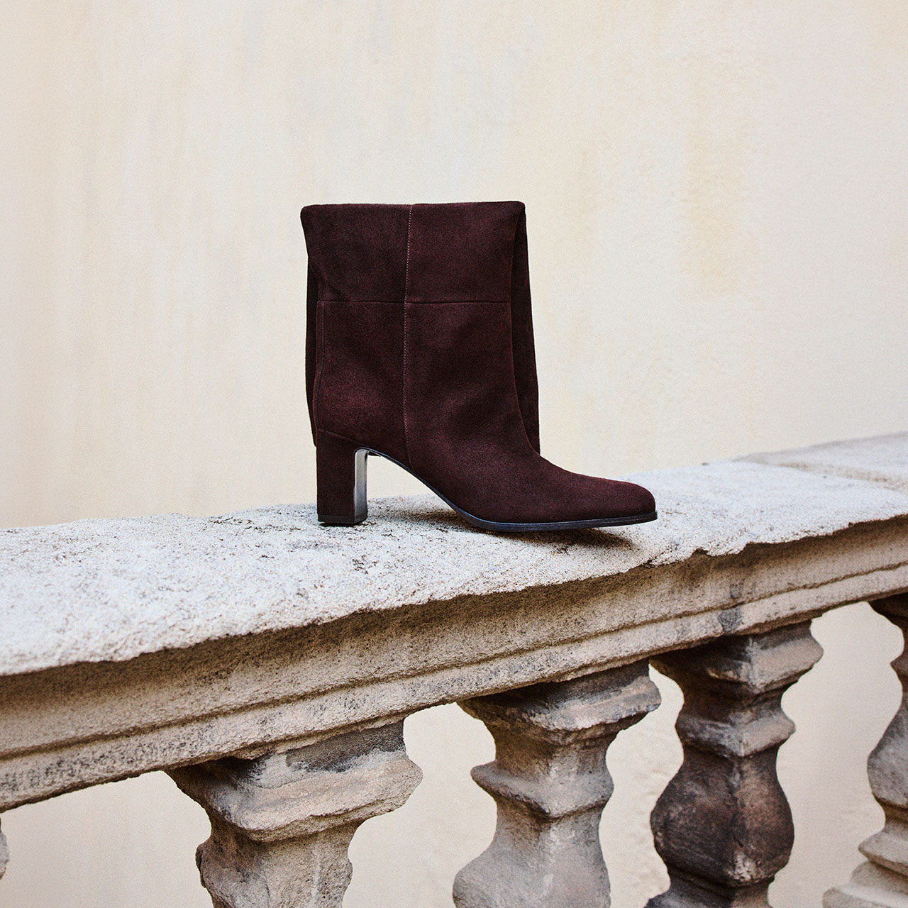 Burgundy suede block heel ankle boot displayed on decorative stone ledge