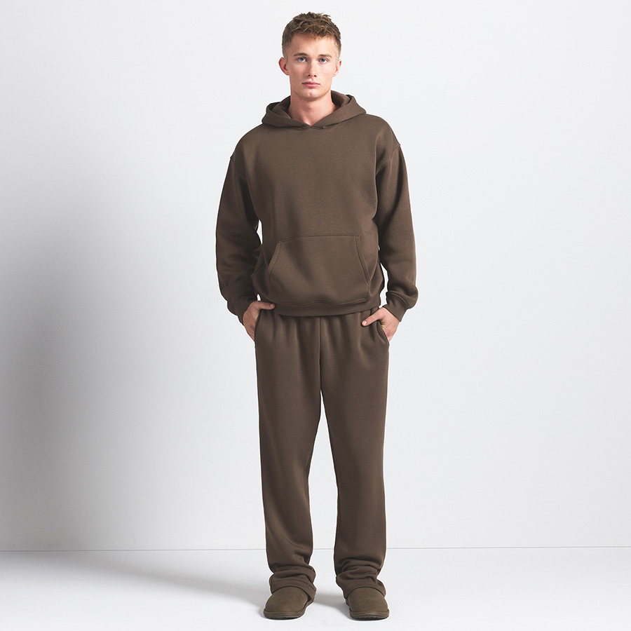 Person in a brown hoodie and sweatpants stands against a white background.