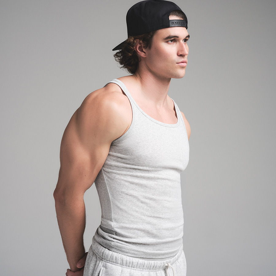 Man in a gray tank top and backward cap stands against a plain background.