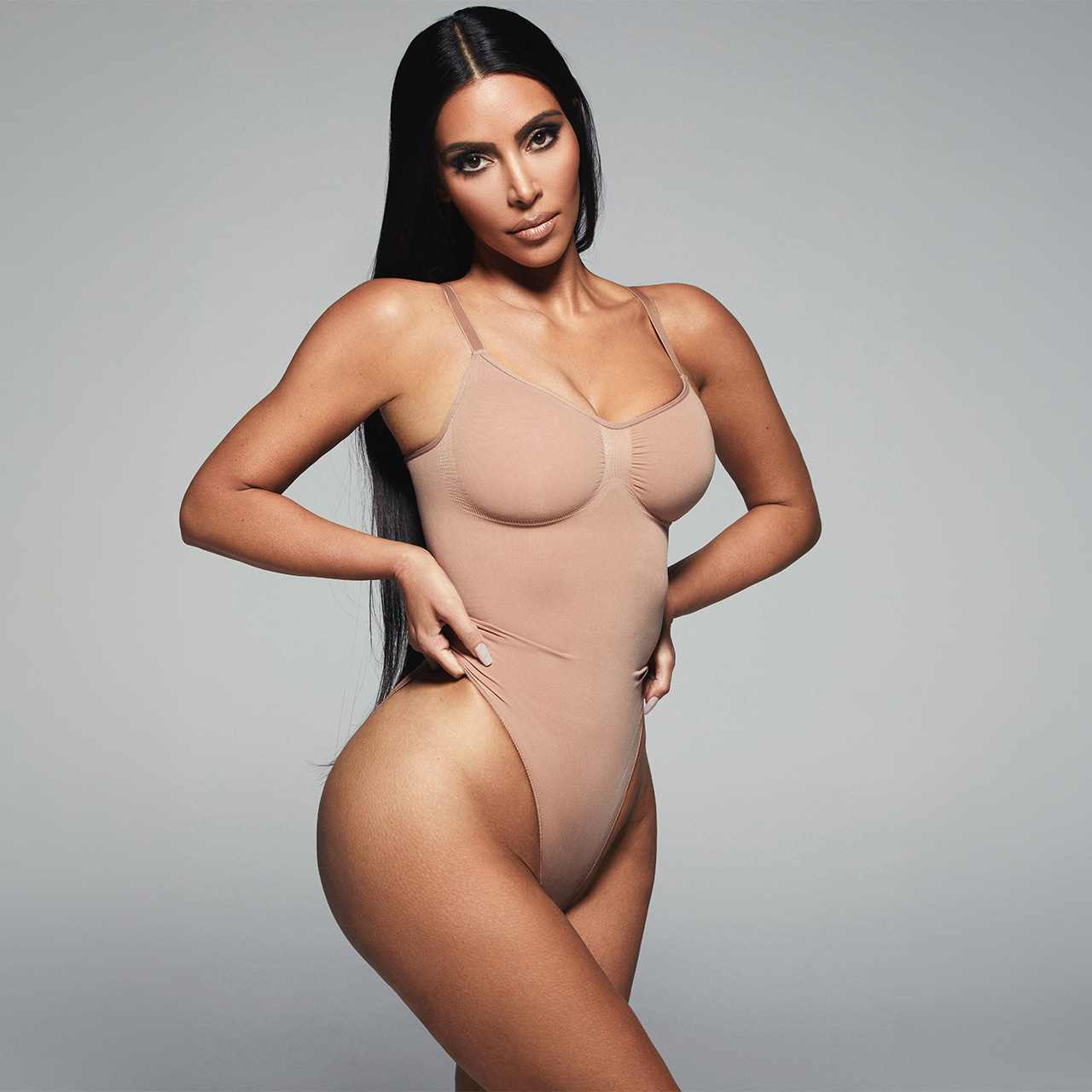 Woman wearing beige seamless sculpting bodysuit against neutral background