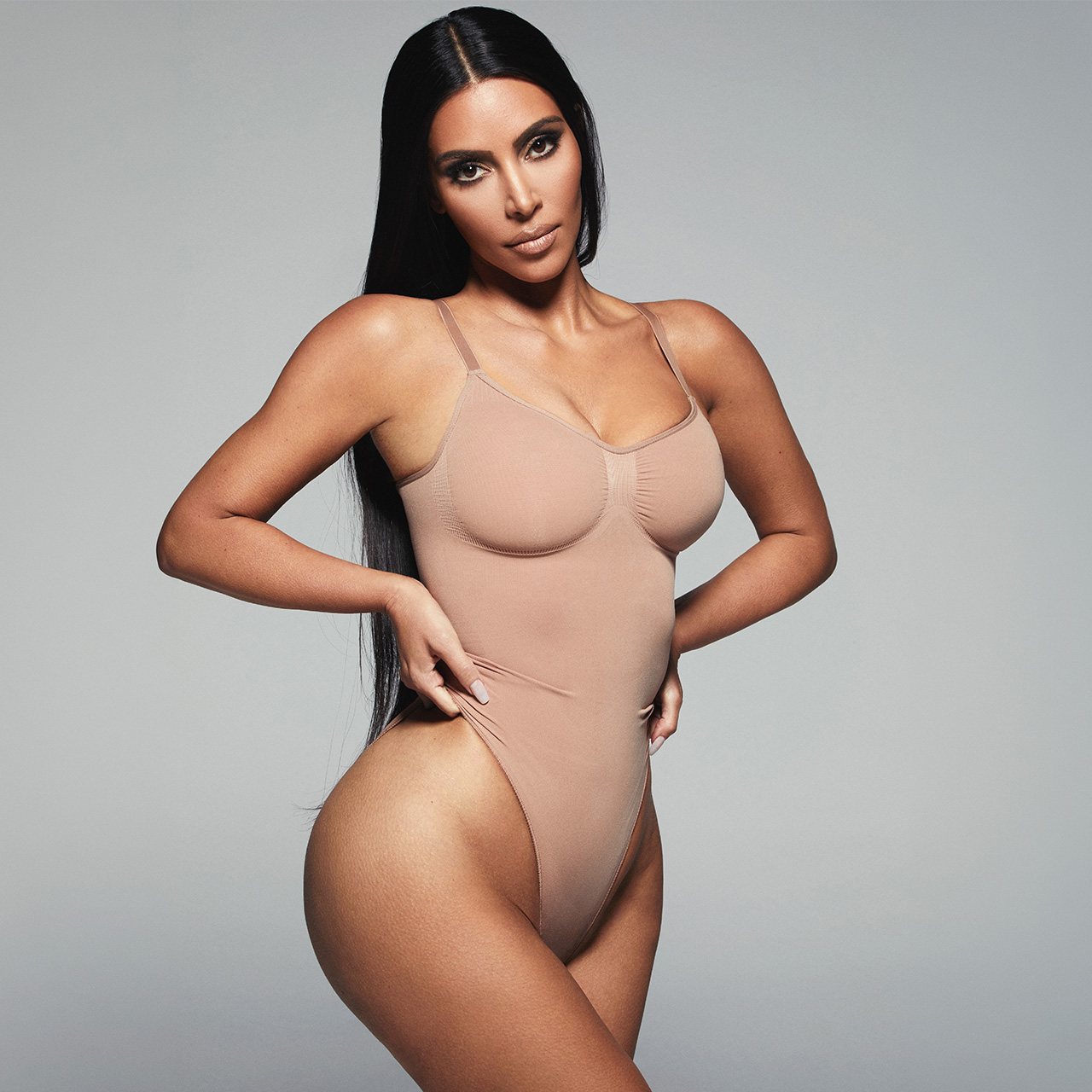 Woman wearing beige seamless sculpt bodysuit with spaghetti straps against neutral background
