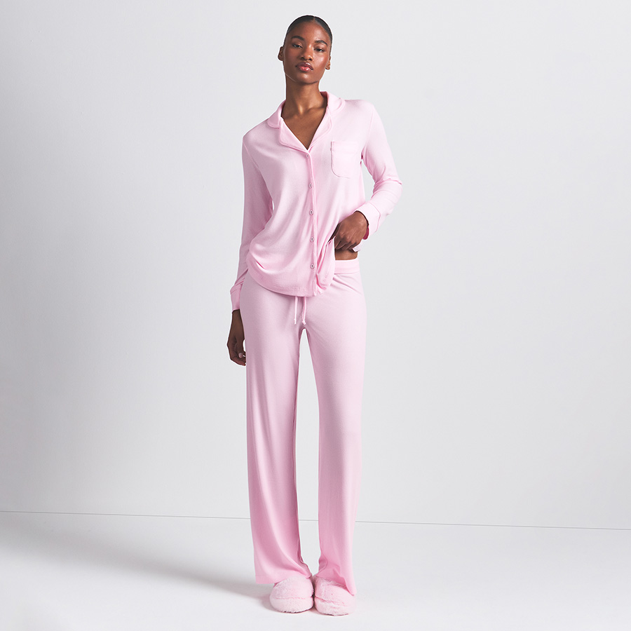 A person wearing a light pink pajama set, standing in front of a plain background.