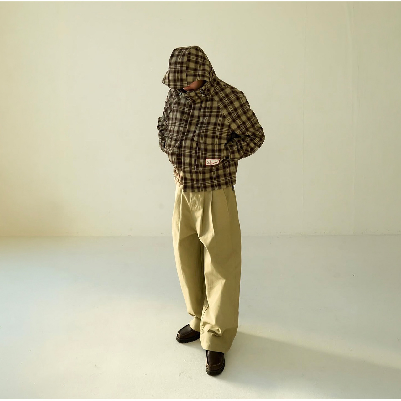 Person wearing olive check hooded jacket with cream trousers and black shoes