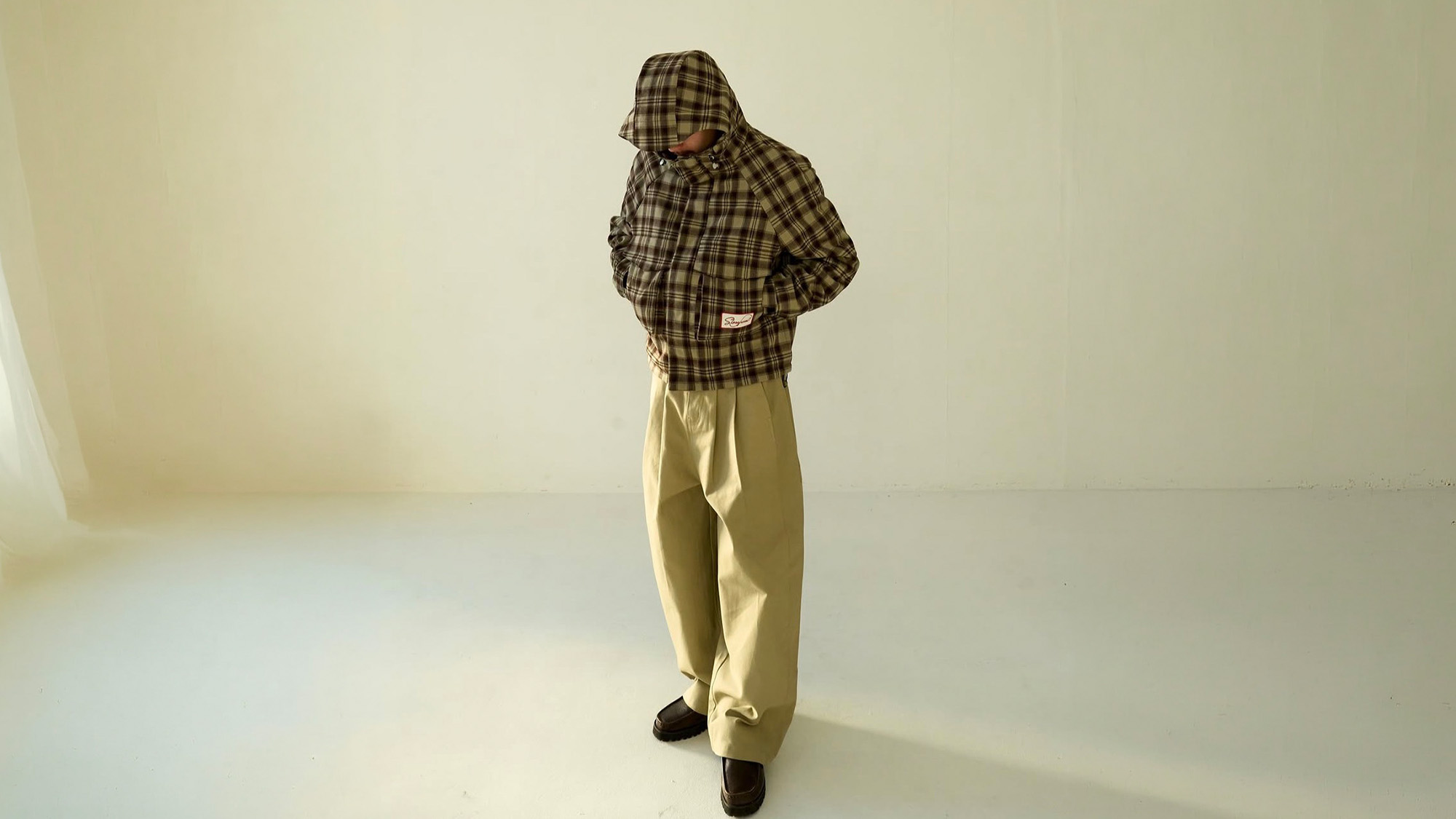 Person wearing olive check hooded jacket with cream trousers and black shoes