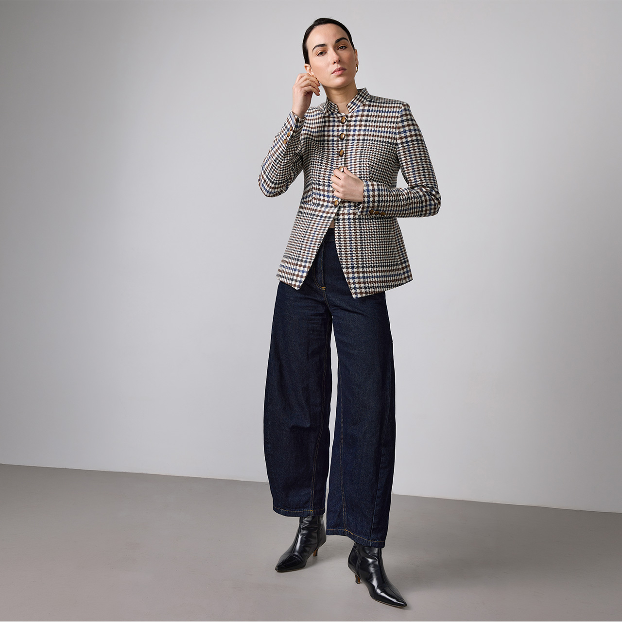 Woman wearing black and white checked blazer with dark navy wide-leg jeans and black ankle boots, standing against neutral background