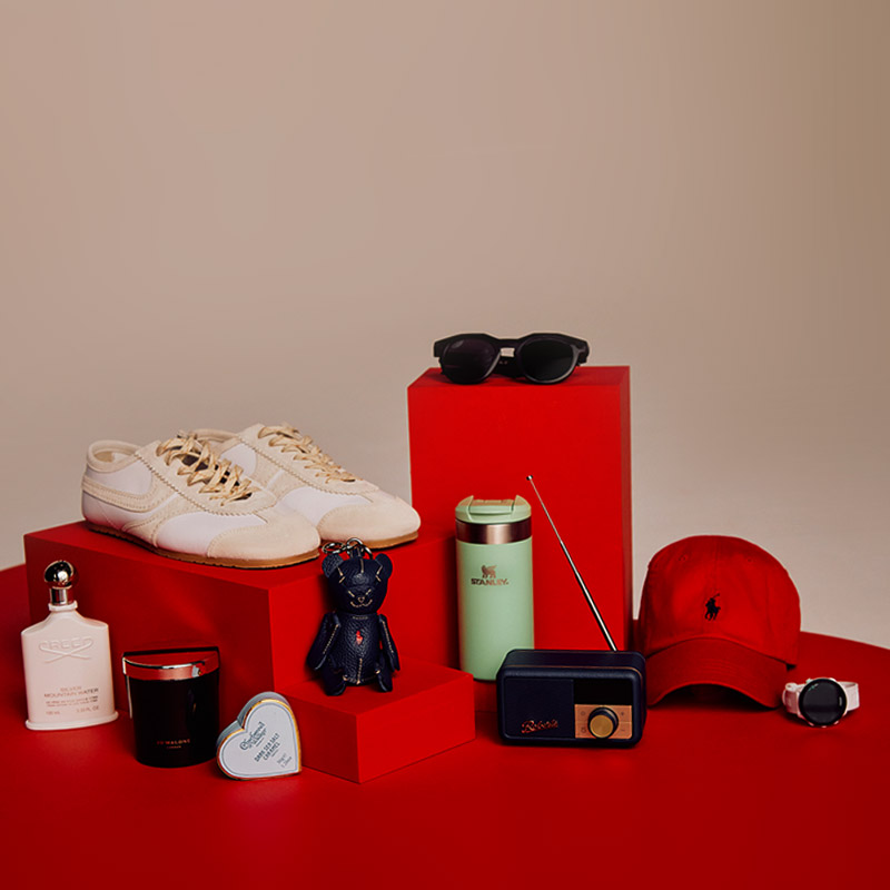 A collection of items including sneakers, sunglasses, a red cap, a thermos, a small radio, a candle, and cologne on red platforms.