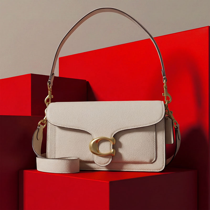 A white handbag with a gold 'C' emblem and adjustable strap is displayed on red geometric blocks.