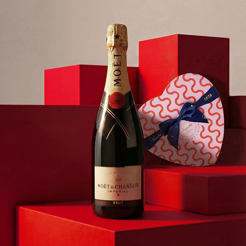 A bottle of Moët & Chandon champagne next to a heart-shaped gift box on red geometric blocks.