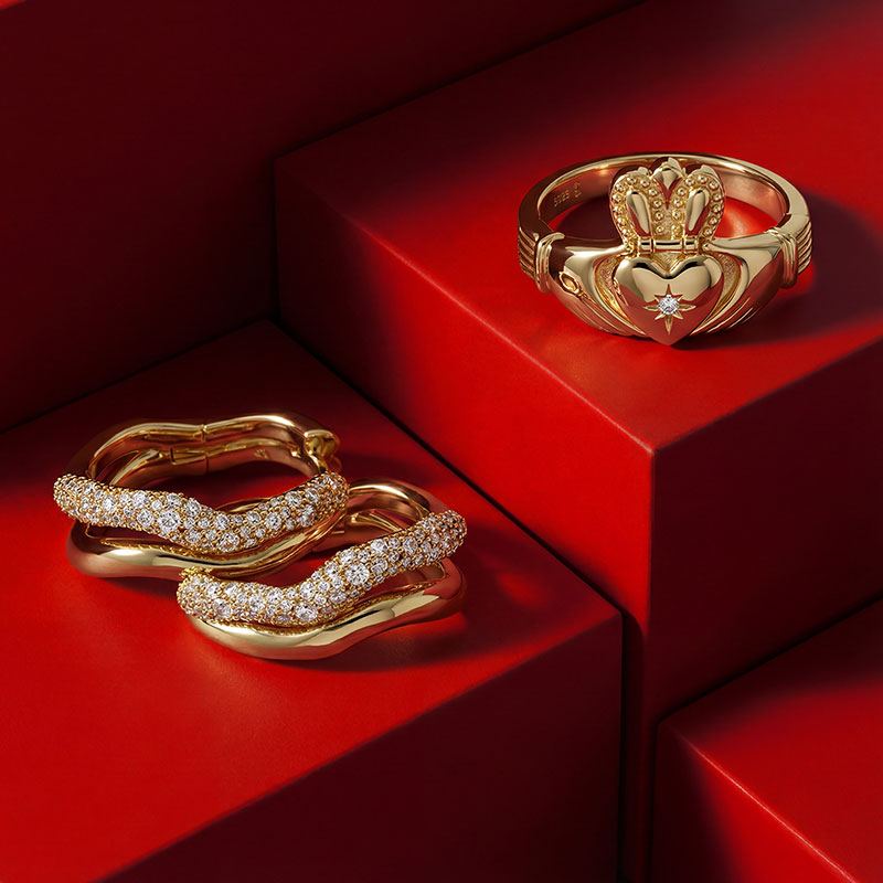 Gold jewelry with intricate designs and diamonds displayed on red geometric surfaces.