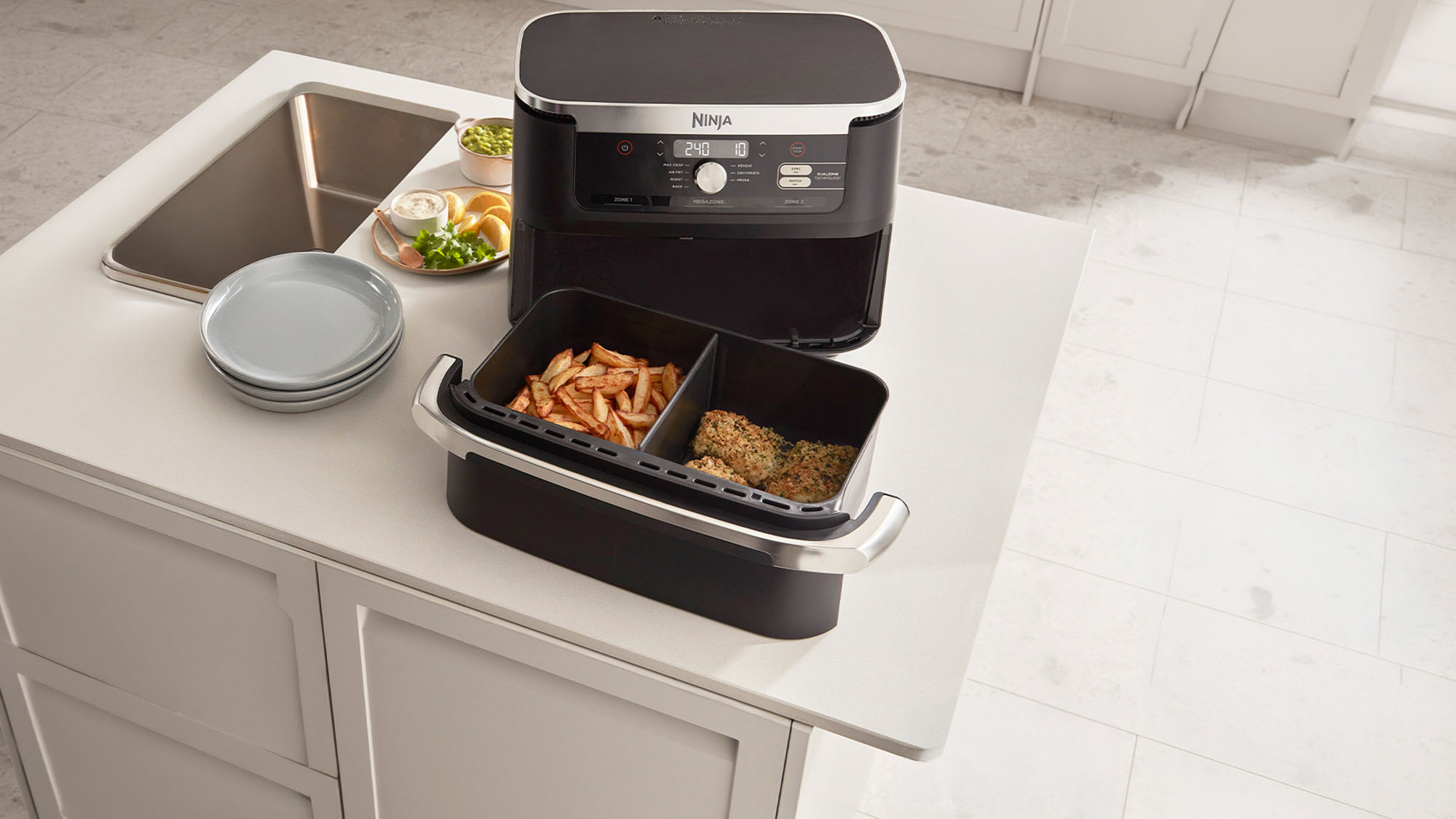 Black and stainless steel air fryer with dual basket showing cooked chips and breaded cutlet, displayed on white kitchen counter