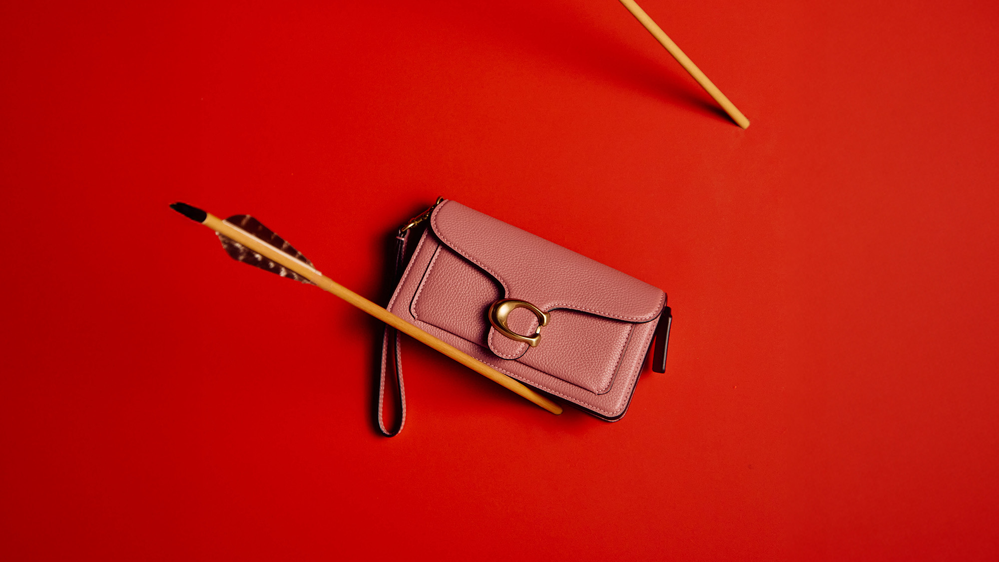 A pink purse with a circular buckle is pierced by an arrow, set against a red background.
