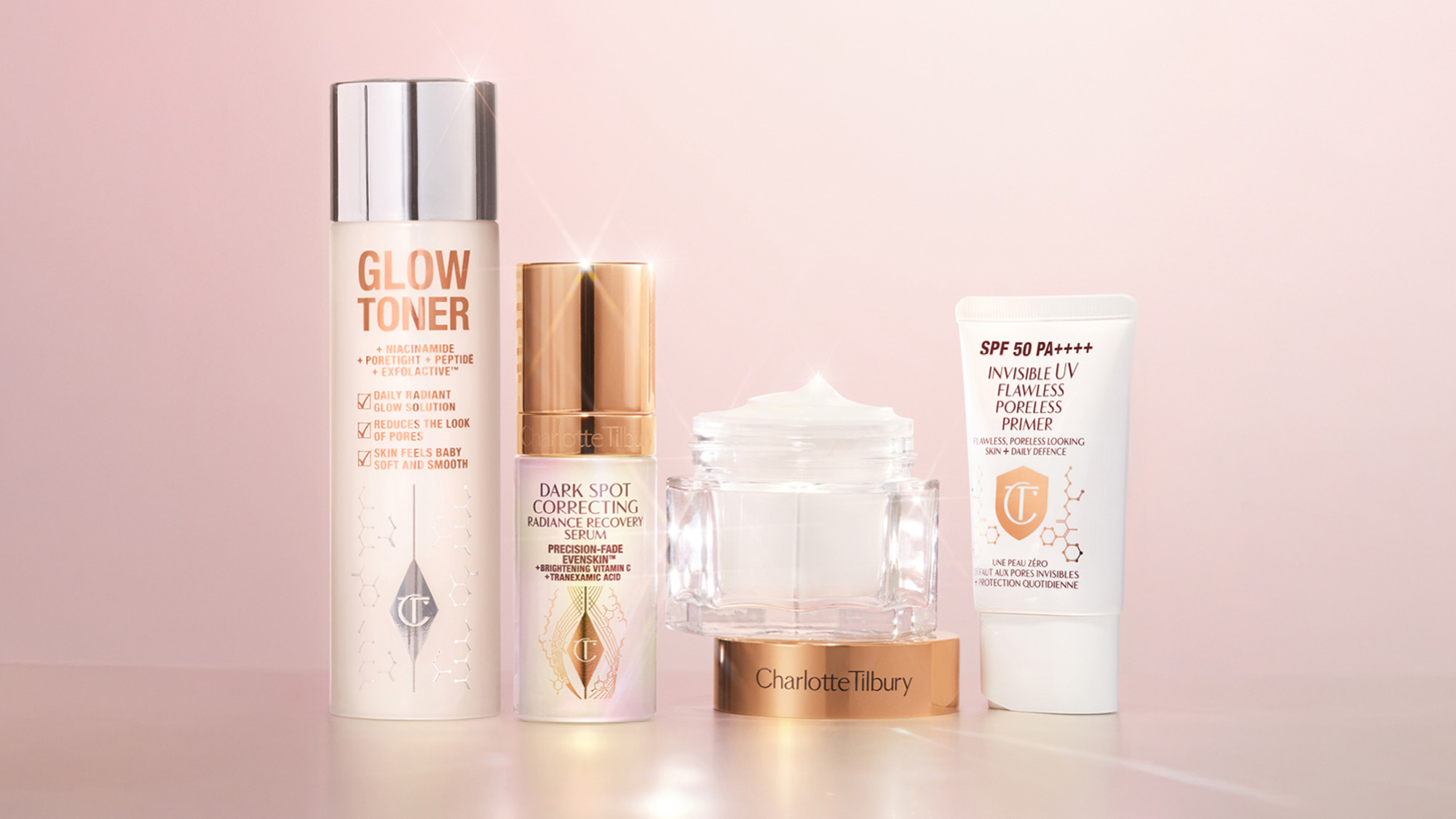 A collection of Charlotte Tilbury skincare products, including a glow toner, dark spot serum, moisturizer, and SPF 50 primer, on a pink background.