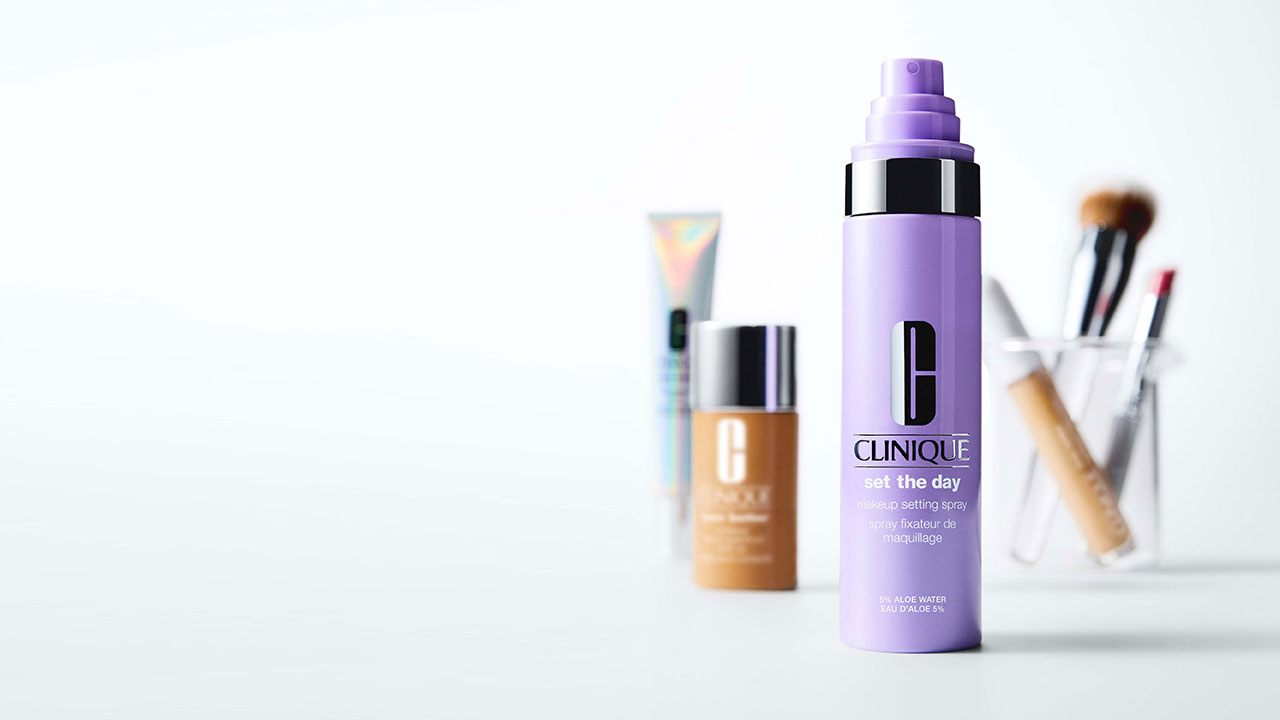 Clinique makeup setting spray bottle in focus, with blurred makeup products in the background.