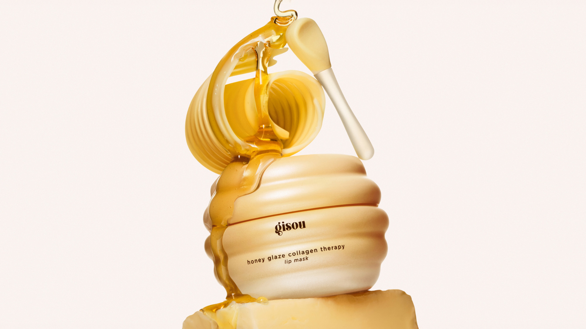 A jar of Gisou honey-infused hair product with honey dripping from a dipper onto the lid.
