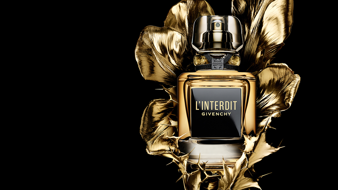A black and gold bottle of Givenchy's 'L'Interdit' perfume surrounded by golden petals.