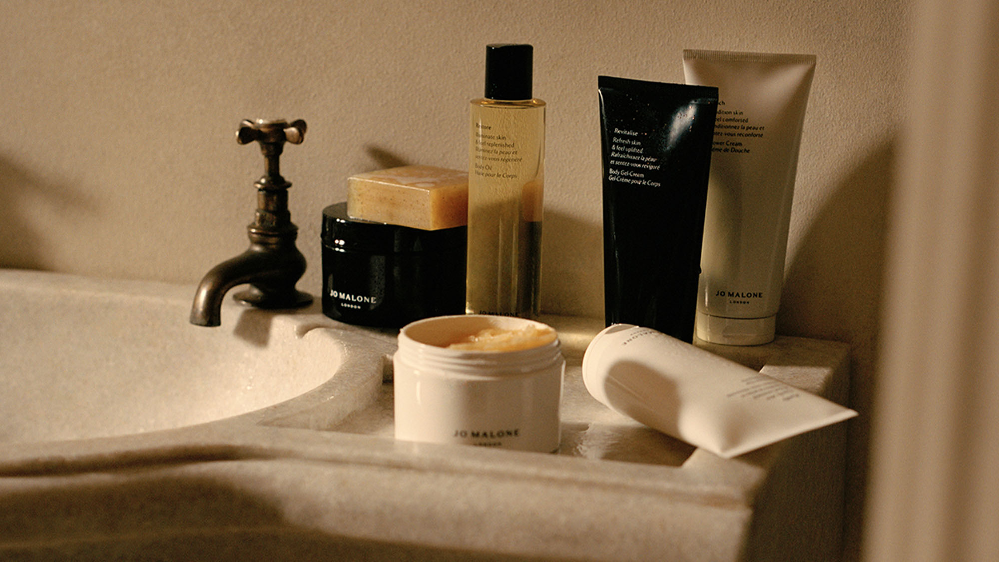 Various skincare products are arranged on a bathroom sink countertop with a vintage-style faucet.