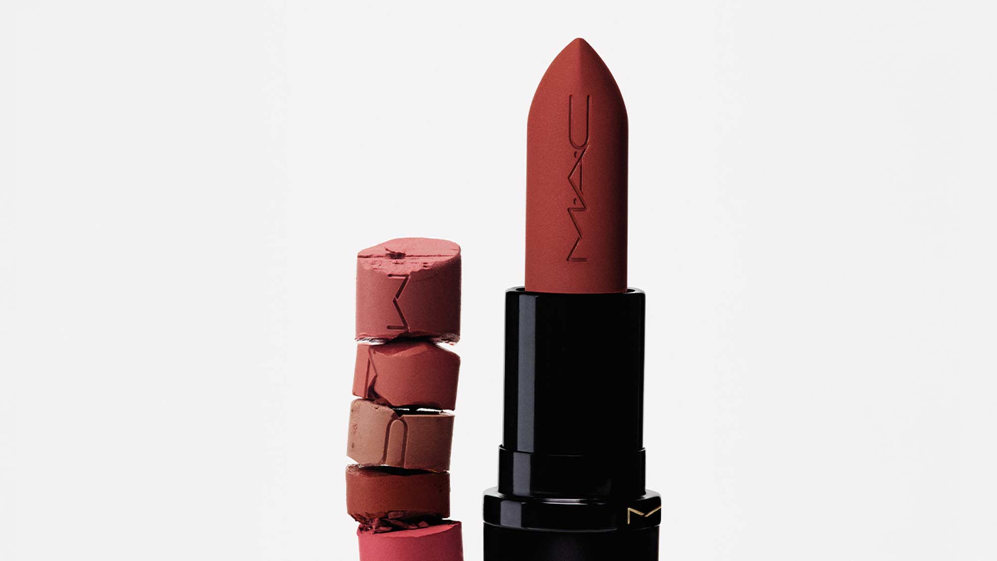 A dark red MAC lipstick beside stacked broken lipstick pieces.