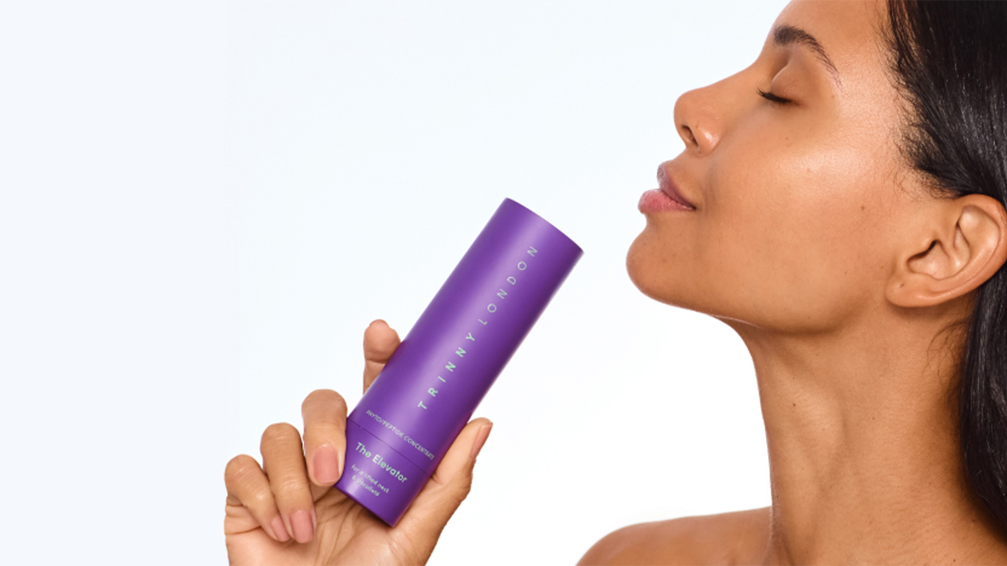 A person holding a purple skincare bottle, smiling with eyes closed.