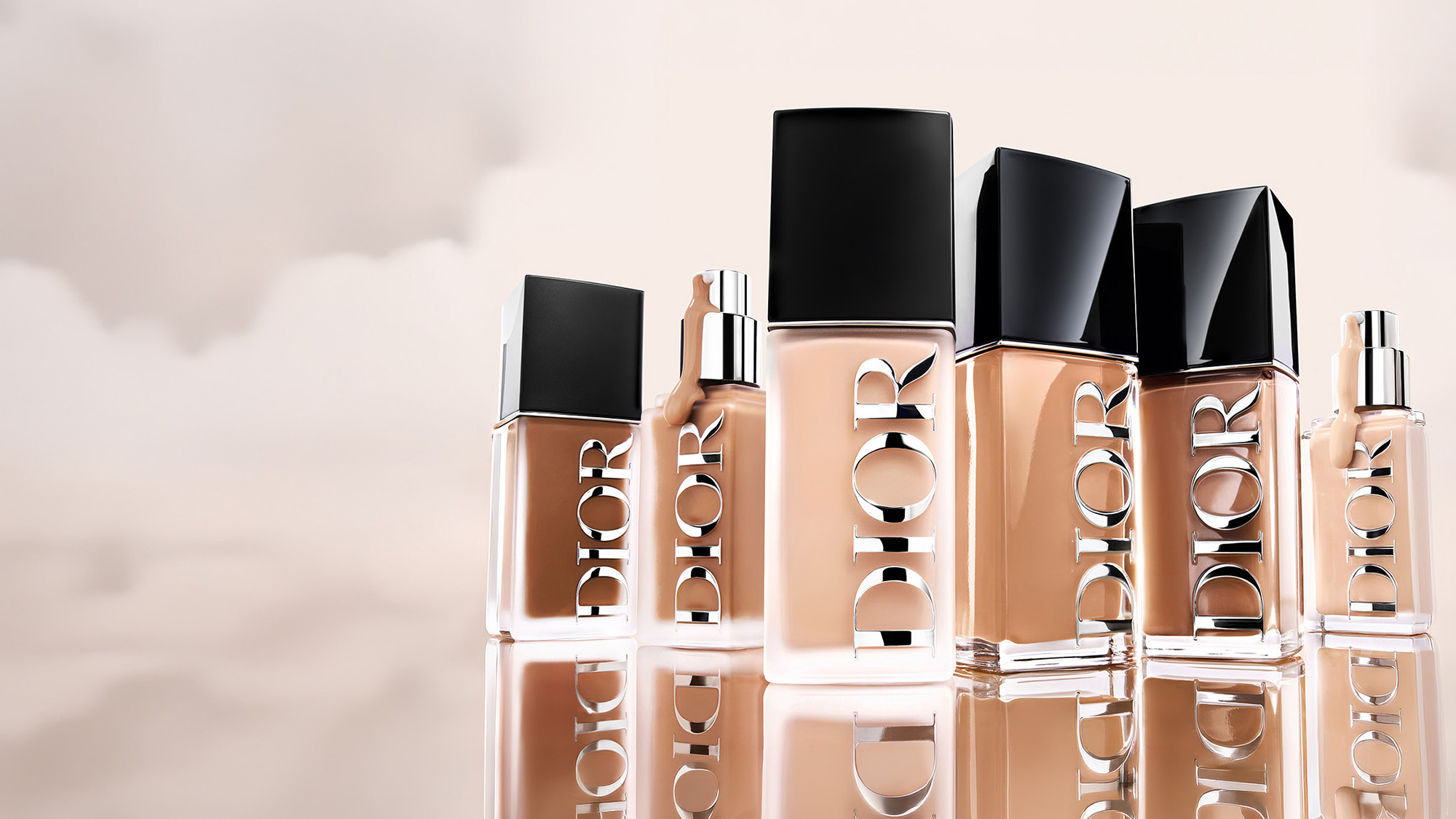 Multiple Dior foundation bottles in various sizes arranged on a reflective surface.