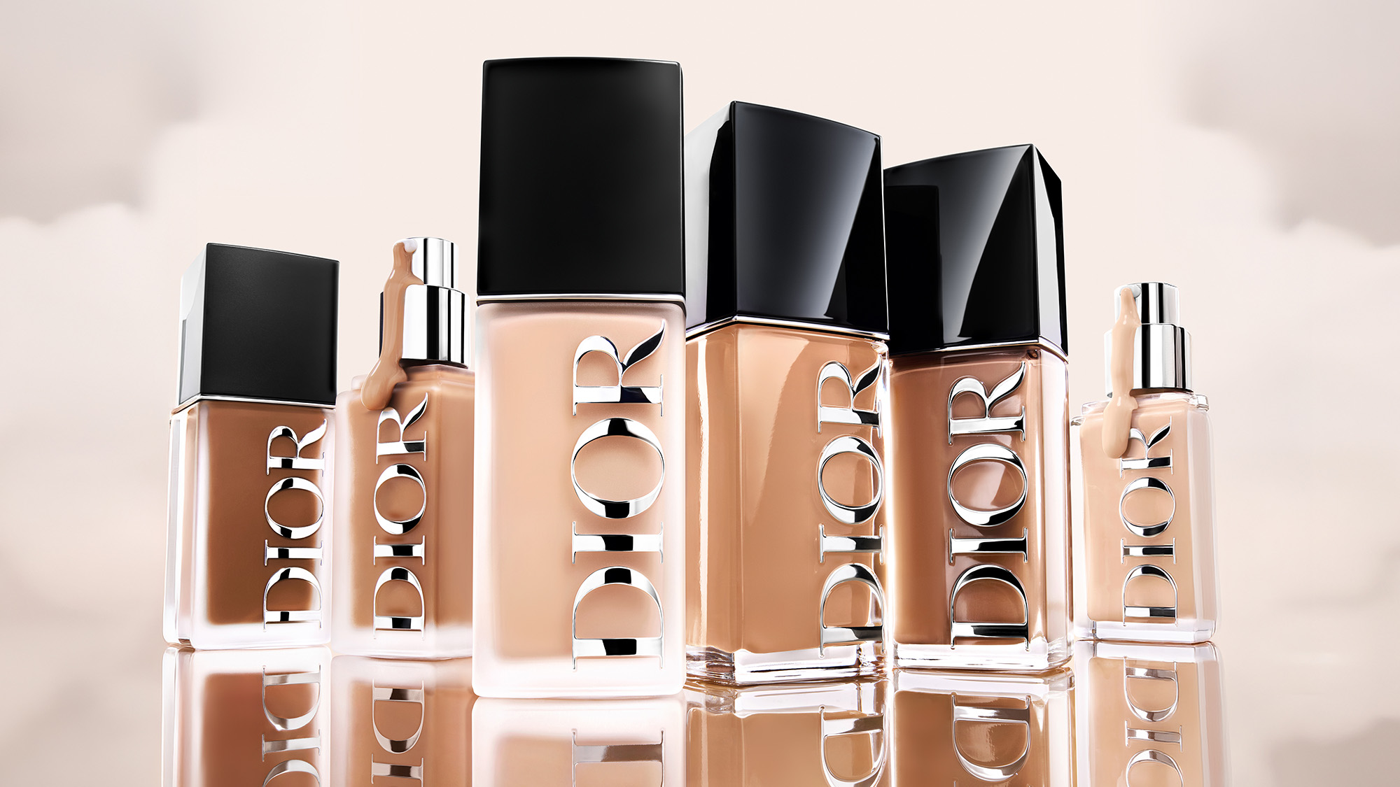 Multiple Dior foundation bottles in various sizes arranged on a reflective surface.