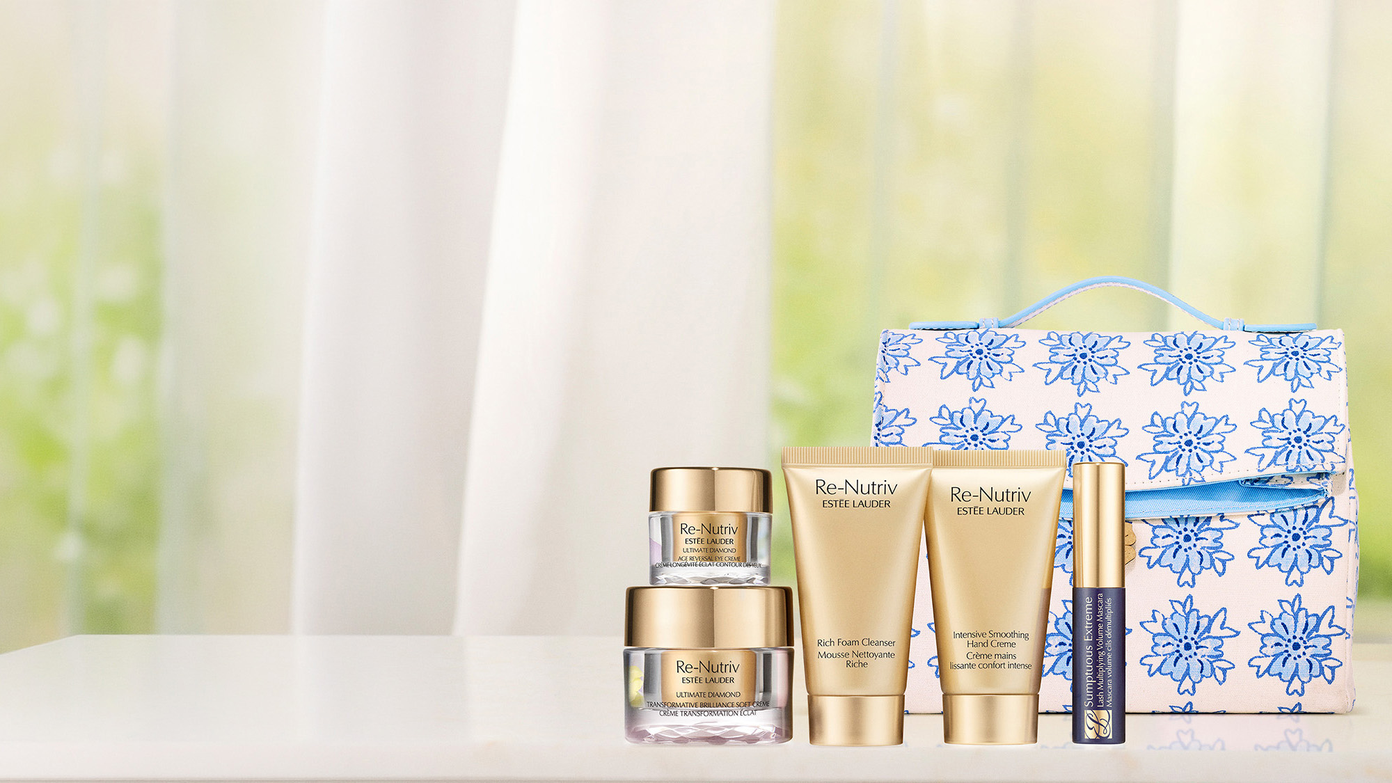 Skincare and cosmetic products with gold packaging arranged on a white surface in front of a floral-patterned bag.