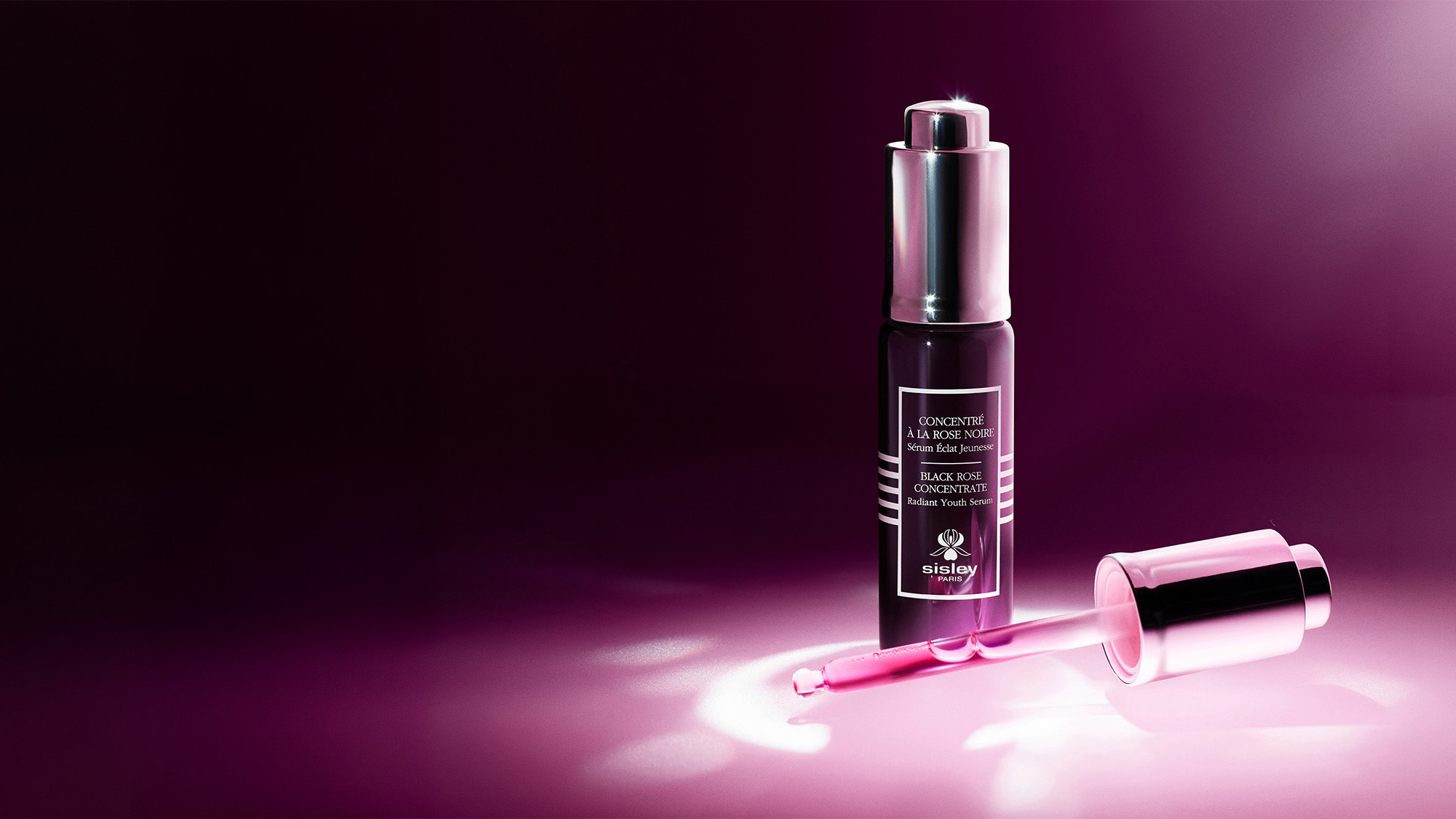 A bottle of Sisley Paris Black Rose Concentrate Serum with a dropper, set against a pink gradient background.