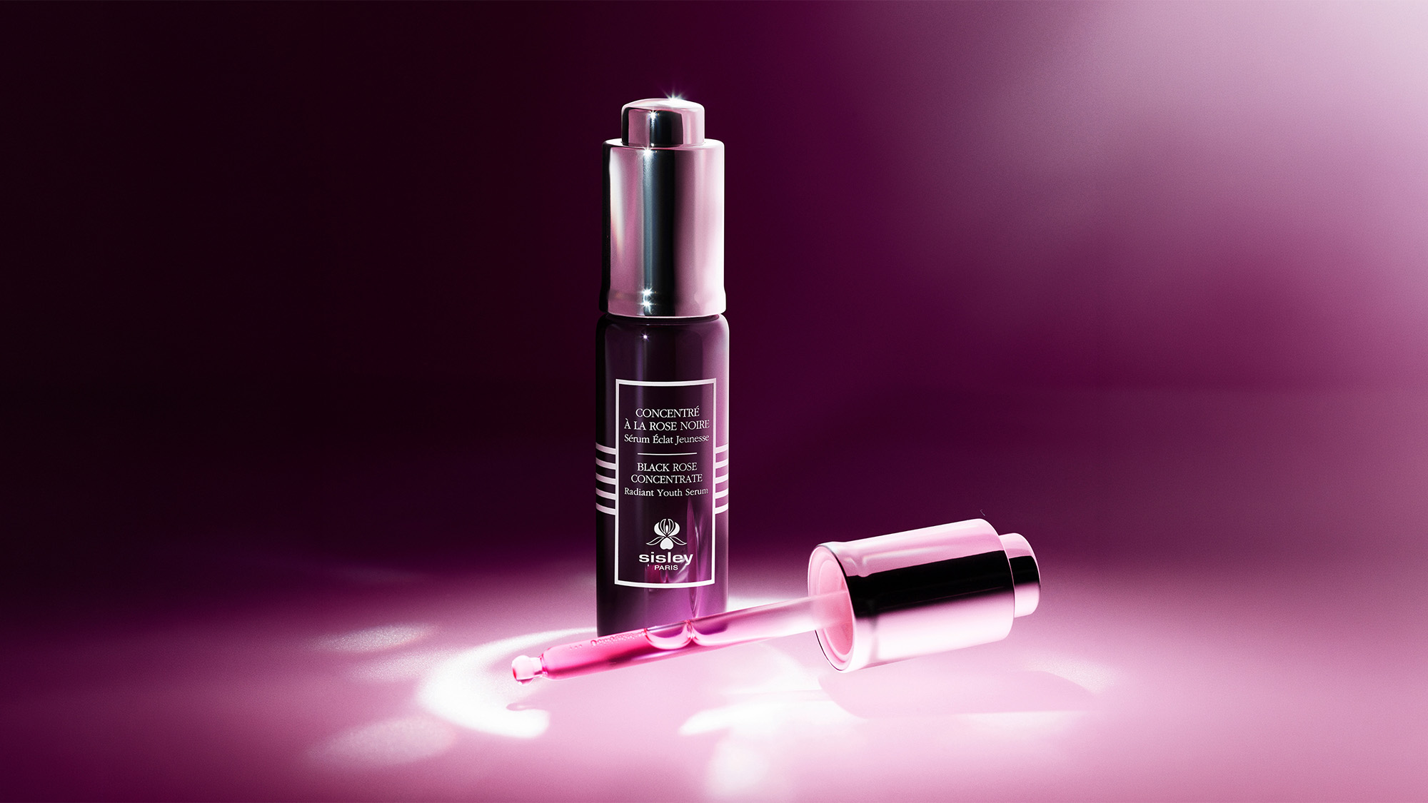 A bottle of Sisley Paris Black Rose Concentrate Serum with a dropper, set against a pink gradient background.