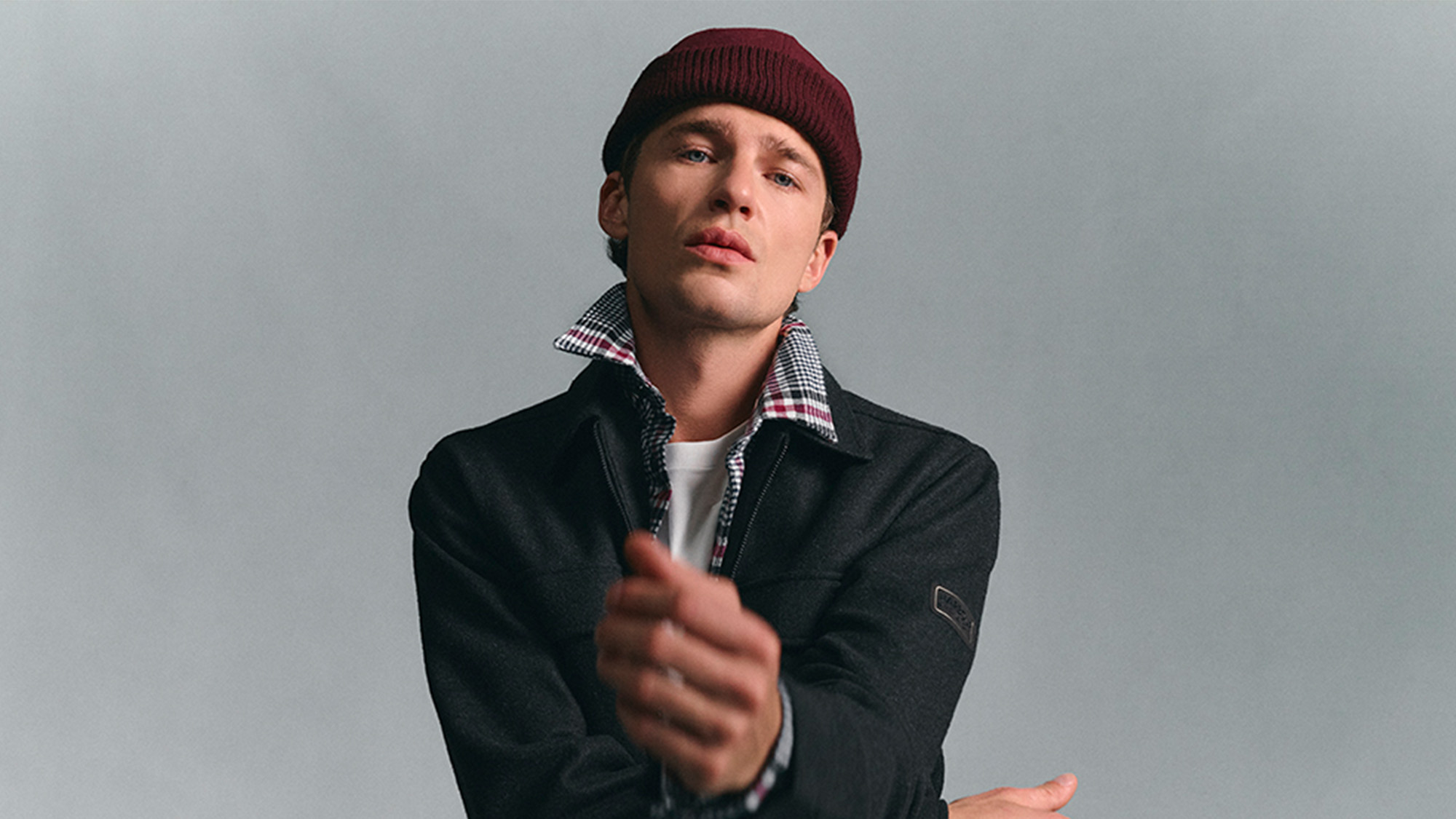 Man in a beanie and jacket poses with a neutral expression against a plain backdrop.