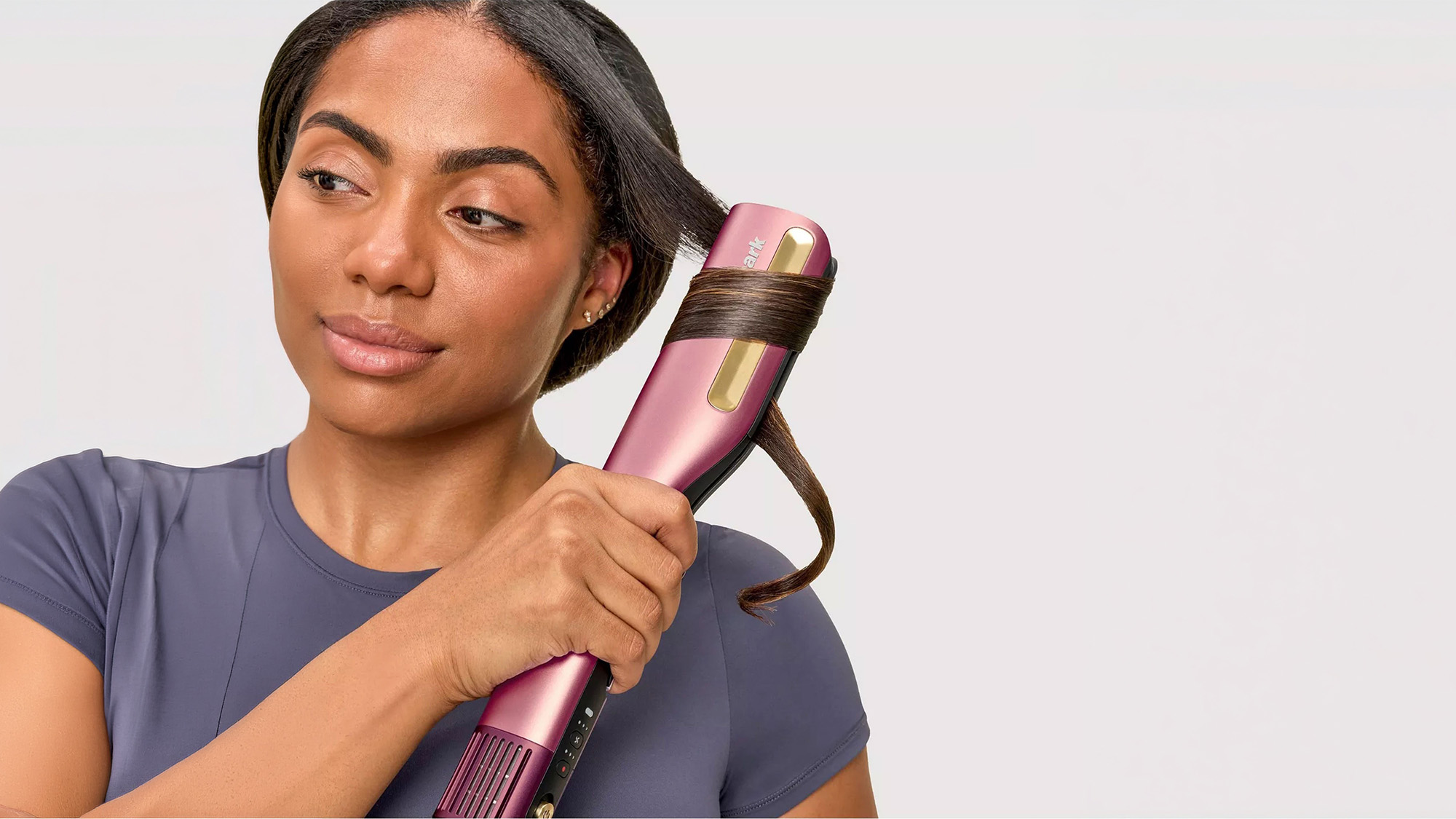 A person uses a pink automatic curling iron on their hair, looking content.