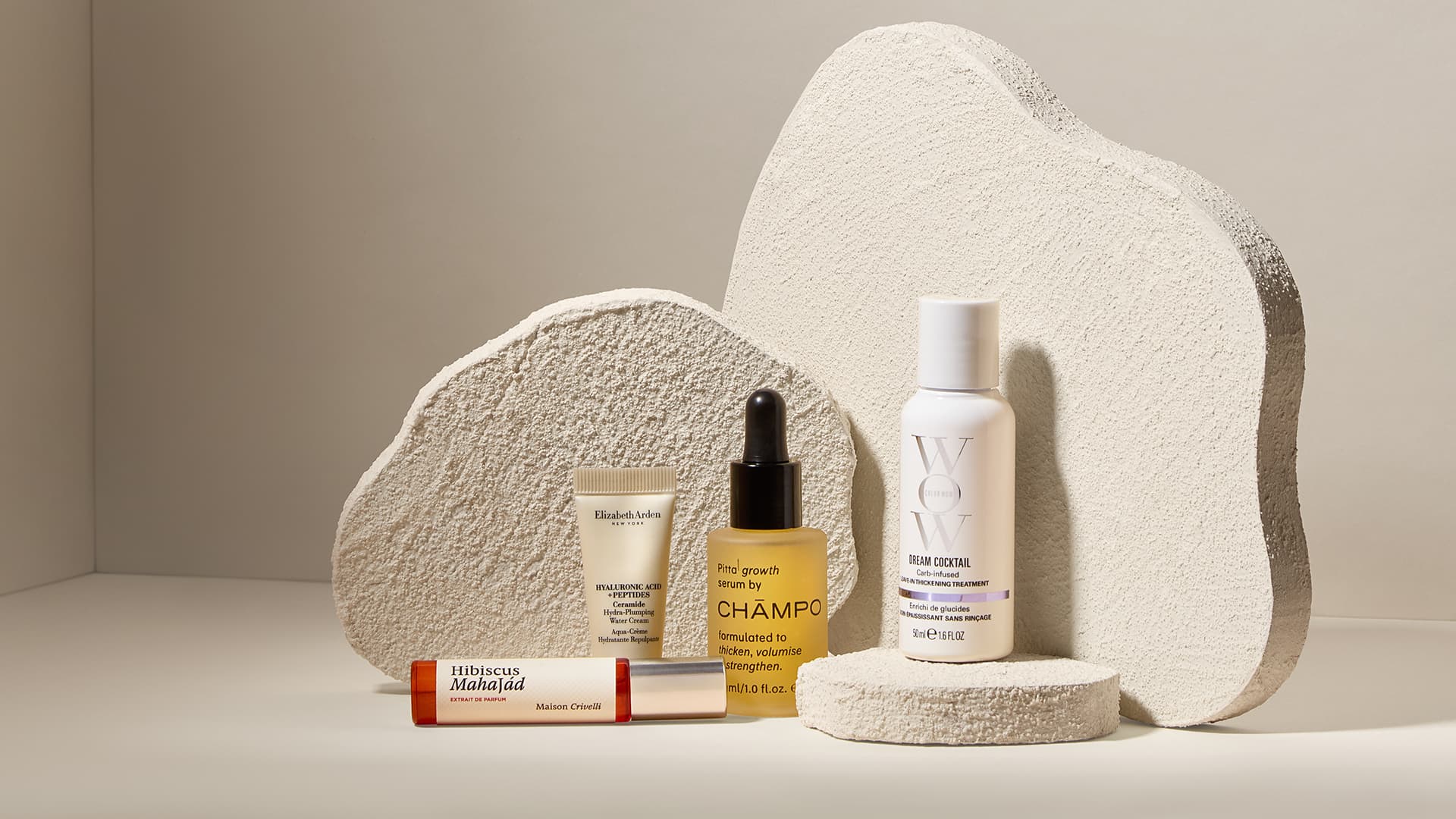 A group of skincare and haircare bottles and tubes are displayed on textured white stands.